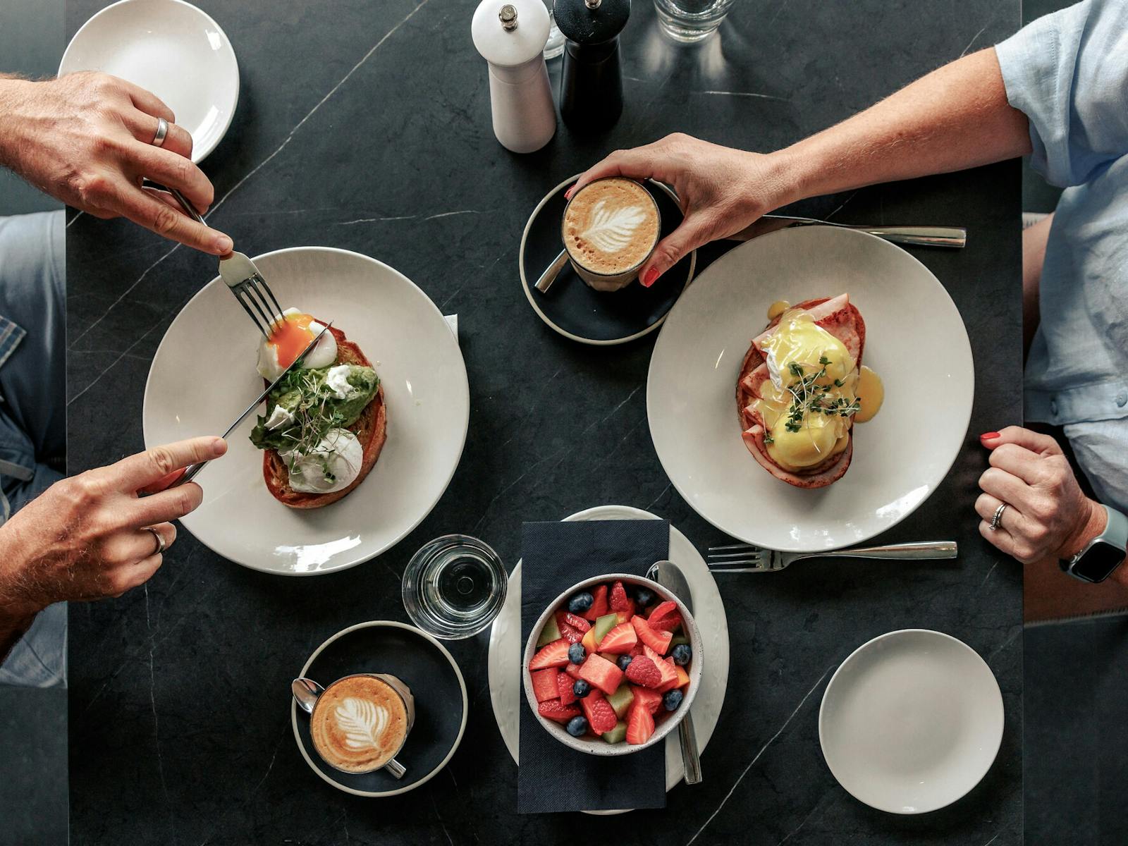 Breakfast dishes enjoyed outdoors showing hands, coffee, fruit and hot cooked egg dishes