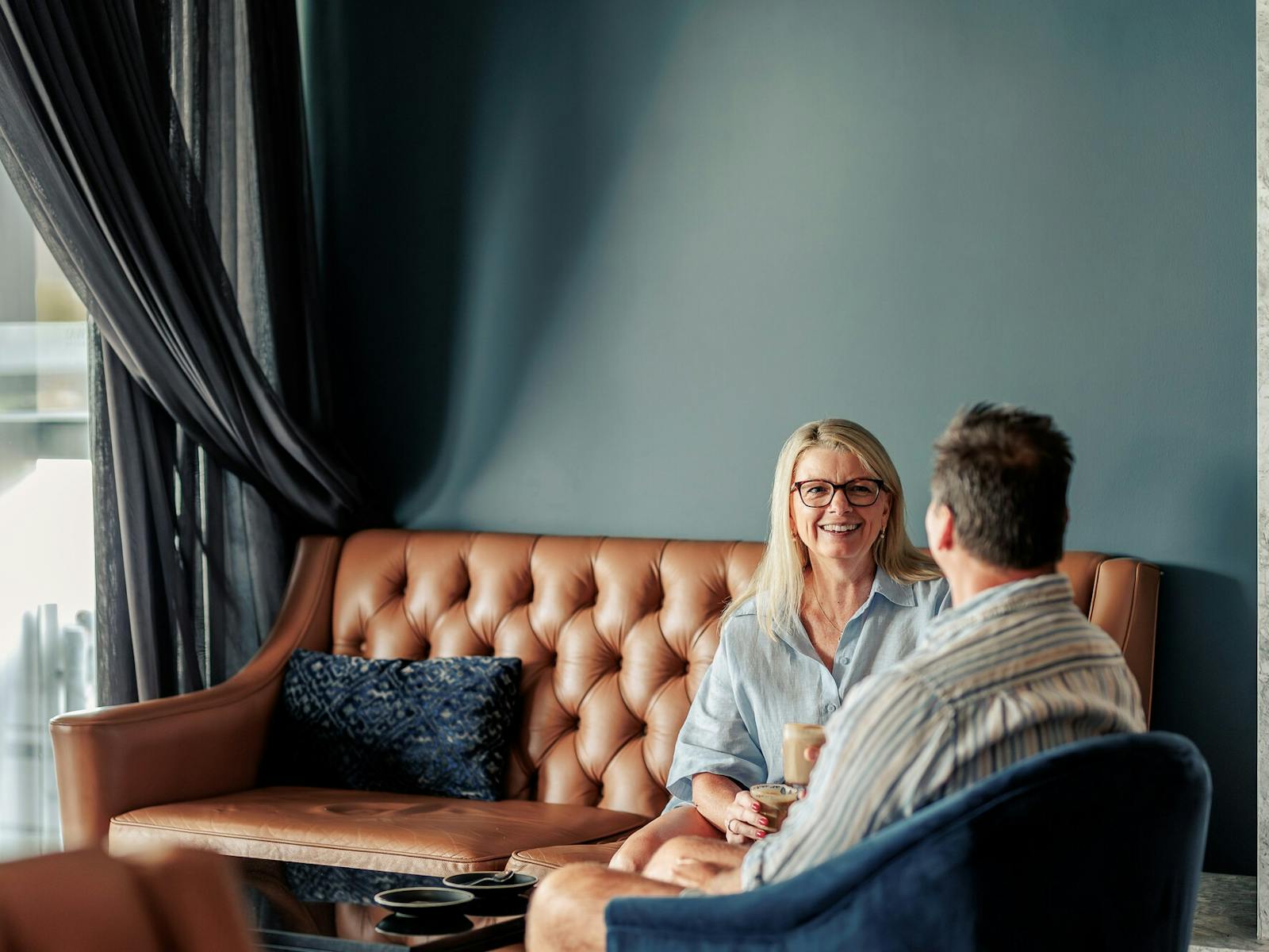 Couple sitting on leather couches chatting in lovely modern lounge of hotel