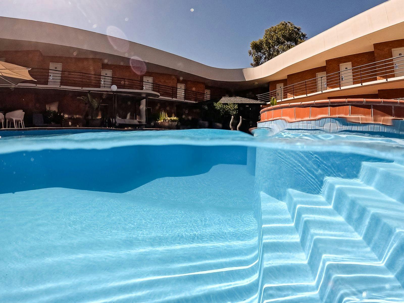 Bright blue swimming pool surrounded by hotel rooms ad landscaped gardens